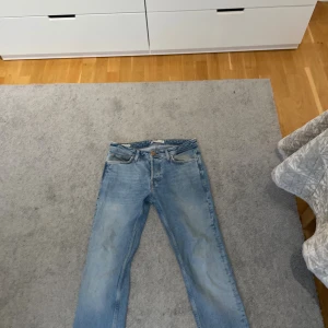 Ljusblå slim straight jeans från Jack and Jones  - Säljer ett par ljusblå jeans från Jack and Jones i modellen Slim Straight Tim. Klassisk femficksdesign, raka ben och snygg tvätt. Jeansen är i bomull och har en stilren look med bruna sömmar och läderpatch bak i midjan.