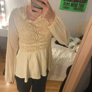 Krämvit spetsblus från Line of Oslo - Superfin krämvit blus från Line of Oslo i storlek S. Blusen har långärmade, lätt transparenta ärmar och ett spetsmönstrat liv med rundad krage. Den har en flowy, peplum-liknande nederdel och är gjord i mjukt, tunt material som känns luftigt och skönt.