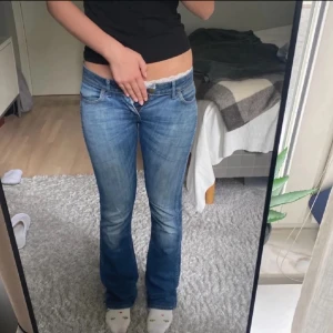 Wrangler bootcut jeans låg midja blå - Säljer ett par klassiska blå jeans från Wrangler med bootcut och låg midja. Jeansen har snyggt slitna detaljer, fem fickor och läderpatch med logga bak. Tillverkade i robust denim med dragkedja och knapp framtill. Som man ser är det slitet vid knappen men det syns ingenting när man har på sig dom. Perfekta till hösten