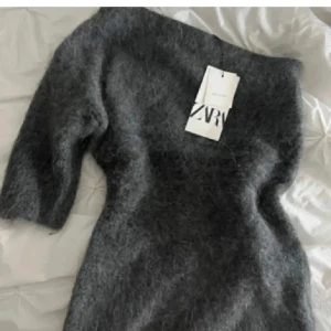 Mörkgrå stickad one shoulder topp från Zara - Supermjuk och fluffig mörkgrå stickad klänning från Zara med trekvartsärm och offshoulder-design. Jättesnygg!!! Använd 1 ggn så mycket bra skick