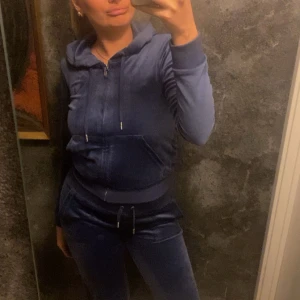 Säljer mitt marin blåa juciycouture sett som jag köpte 2024 ocj andvänt Max 15 gånger  - Mysig blå hoodie i velour med huva, dragkedja och snörning. Tröjan har långa ärmar, ribbade muddar och en stor ficka framtill.  Med sköna byxor till.