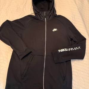 Svart Nike Air Max hoodie size M - Svart Nike Air Max hoodie med hel dragkedja, huva med snörning och vita logotyper på bröstet och ärmen. Praktiska fickor framtill och sportig look. 