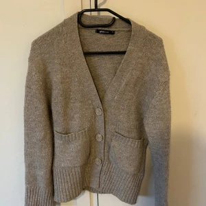 Beige kofta från Gina Tricot XS - Mysig beige kofta från Gina Tricot i stickat material. Modellen har v-ringad hals, tre knappar framtill och två stora fickor. Ribbstickade muddar vid ärmslut och nederkant. Supersnygg och slutsåld. OBS köp helst inte via Bring!