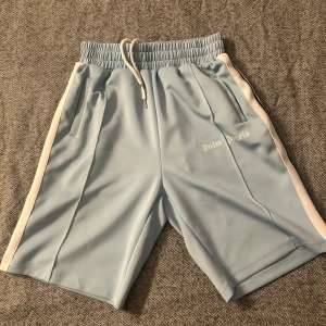 Palm Angels shorts - Palm Angels shorts i ljusblått med vita sidoränder och svart detalj. Storlek M (stor i storleken) Använd ett par gånger men inget som syns på plagget, hör av dig om du har frågor😊