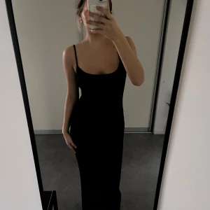Svart långklänning med smala axelband - Säljer en svart långklänning med smala axelband och figurnära passform. Klänningen har en enkel och stilren design med rundad urringning och ärmlös siluett. Perfekt för dig som gillar minimalistisk och elegant stil.