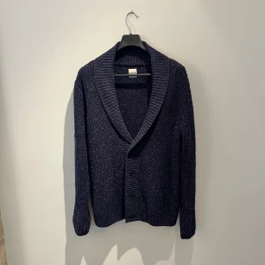 Mörkblå stickad kofta från KIOMI - Säljer en mörkblå stickad kofta från KIOMI med grov ribbad krage och tre knappar framtill. Koftan har långärmad passform och är tillverkad i ett mjukt stickat och exklusivt material som känns riktigt skönt. Perfekt för dig som gillar chill och stilren look. Hör av er vid frågor eller fler bilder