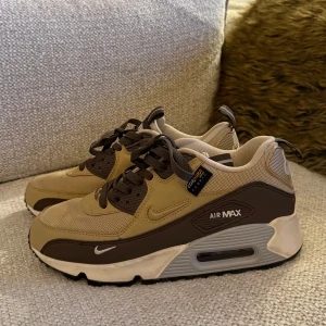 Nike Air Max 90 - Nike Air Max 90 sneakers med Cordura-material i snygg brun och beige färg. Klassisk siluett med synlig Air Max-dämpning, mesh och syntet på ovandelen, bruna snören och detaljer. Perfekt för dig som gillar streetwear och vill sticka ut med en unik färgkombo. 
