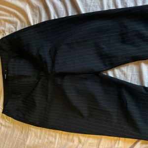 Svarta randiga kostymbyxor Bik Bok - Snygga svarta kostymbyxor från Bik Bok med tunna vita ränder. Klassisk rak passform/bootcut och perfekta för en stilren look. Materialet känns mjukt och följsamt. Världens skönaste byxor i midwaist/highwaist💞