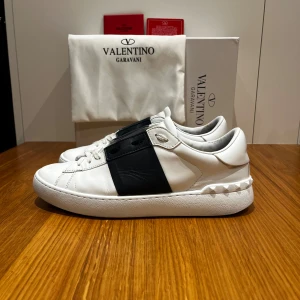 Valentino Garavani Open - Ett par vita valentino skor med marinblå rem över mitten (ser svart ut på bilden men är blå i verkligheten). Väldigt litet hål i bak på hälen, men läcker inte in eller något sådant. Hör av er vid intresse!