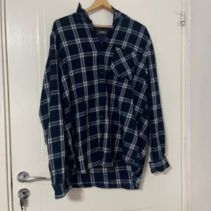 Blårutig henley skjorta från Max  - Blårutig henley skjorta från Max i storlek XL. Skjortan har ett klassiskt rutmönster i mörkblått och vitt, lång ärm och knappstängning framtill. Materialet är mjukt och består av 85% bomull och 15% viskos. Bröstficka med sned rutmönster för extra stil.