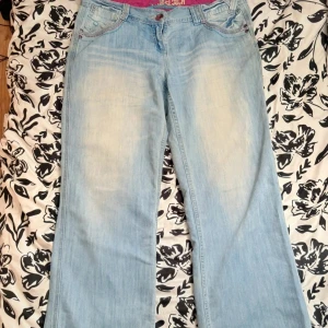 Low waist 200s jeans  - Ett par ljus blå low waist jeans som är lite baggy! Men coola detaljer på fixorna! Skönt material!!  Midja: 46/47 cm står storlek 42 uk 14! Skriv om du har några frågor eller är intresserad! 
