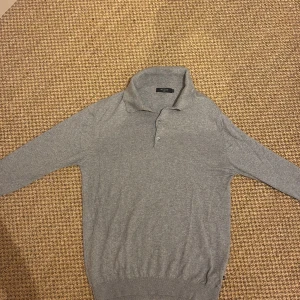 Grå pikétröja från Matinique - Säljer en stilren grå pikétröja från Matinique i storlek M passar även S. Tröjan har klassisk krage, knäppning med två knappar och är långärmad. Perfekt för dig som gillar en clean och enkel look..