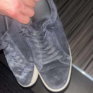 Mörkblå mockasneakers med snörning - Säljer ett par mörkblå sneakers i mocka med klassisk snörning och vit sula. Skorna har en stilren och enkel design som passar till det mesta. Perfekta för dig som gillar en clean look med lite extra känsla tack vare mockamaterialet.