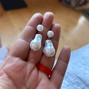 pärlörhängen - Säljer ett par coola örhängen med stora, oregelbundna vita pärlor och mindre pärlor upptill. De har en elegant och modern vibe, perfekt för dig som gillar statement-smycken. Fästet är i guldton och pärlorna har en snygg glans.