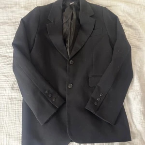 Svart kavaj från Bik Bok - Klassisk svart kavaj från Bik Bok med två knappar framtill och fickdetaljer. Snyggt skräddad passform och helfodrad insida. Perfekt för en stilren look och enkel att matcha med olika outfits.