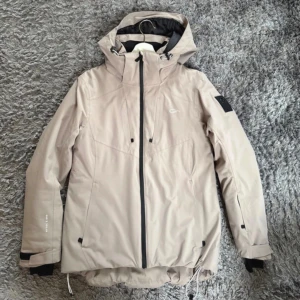 Beige skidjacka från Five Seasons - Snygg beige skidjacka från Five Seasons i mycket bra skick. Har bland annat ficka för skidkort i ärmen och snölås. Vattentät för 5.000 mm. Vindtät.
