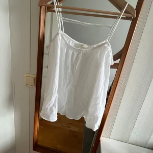 Vit linnetopp med smala axelband - Fräsch vit linnetopp från H&M med smala dubbla axelband och lätt rynkad struktur i tyget. Toppen är ärmlös och har en luftig passform. Enkel och stilren design som funkar till många looks.