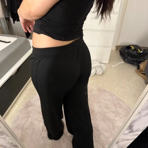 Svarta ribbade mjukisbyxor wide - Svarta mjukisbyxor med ribbad struktur och bred resår i midjan. Modellen är loose och har ett wide snitt som ger en avslappnad vibe. Materialet är mjukt och stretchigt, perfekt för chill dagar. Snygga att matcha med en crop top eller hoodie.