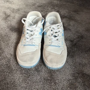 New Balance 550 sneakers vit/blå - Säljer ett par New Balance 550 sneakers i vitt och ljusblått. Skorna har klassisk snörning, platt sula och detaljer i mocka och skinn. Perfekta för dig som gillar retrostil och vill ha något som sticker ut lite extra. Skorna är storlekt 43 men är små i storleken så skulle säga att dom passar om du har storlek 42.