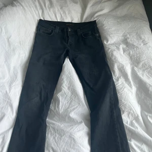  Nudie Jeans - Säljer ett par mörkblåa jeans från Nudie Jeans med klassisk femficksdesign och snygg vågdetalj på bakfickan. Jeansen har raka ben och slim passform. Perfekta för dig som gillar stilrena och tidlösa jeans.