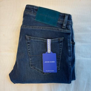 Jacob Cohën Nick jeans mörkblå helt nya - Jacob Cohën Nick jeans i mörkblå tvätt med klassisk femficksdesign och snygga detaljer som blå knapp och märkesskylt i mocka. Jeansen har rak passform och är tillverkade i mjukt stretchigt denim för extra komfort. Made in Italy.
