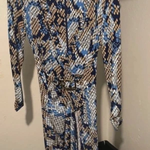 Mönstrad långklänning med bälte - Snygg långklänning med coolt mönster i blått, beige och svart. Klänningen har lång ärm och ett matchande bälte i midjan som ger en schysst siluett. Perfekt för dig som gillar att sticka ut med unika prints och vill ha en bekväm men trendig look.