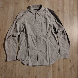 Ljusblå skjorta från Ralph Lauren - Klassisk ljusblå skjorta från Ralph Lauren med button-down krage och broderad logga på bröstet. Skjortan har långa ärmar, knappar framtill och är tillverkad i ett mjukt bomullstyg. Perfekt för en clean och stilren look. Nypris: va 1500