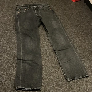 Levi's 501 svarta jeans W30 L30 - Säljer ett par klassiska svarta Levi's 501 jeans med raka ben och normal passform. Jeansen har fem fickor, knappgylf och den ikoniska läderpatchen bak i midjan. Perfekta för dig som gillar en tidlös look och vill ha ett par jeans som funkar till allt.