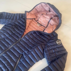 Mörkblå Colmar pufferjacka - Snygg mörkblå pufferjacka från Colmar med ljusrosa insida och huva. Storlek 44. i stort sätt oanvänd. Perfekt nu när det börjar bli lite kallare.