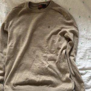 Beige stickad tröja från Morris - Snygg beige stickad tröja från Morris med rund hals och diskret broderad logga på bröstet. Tröjan har långärmad passform och ribbade muddar vid ärmslut och nederkant. Perfekt för dig som gillar stilrena och klassiska plagg. Den är aldrig använd. Den är liten på mig därför säljs den. Den passar S mer skulle ja Säga