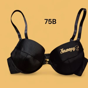 Ny! Svart Snoopy behå 75B - Svart behå med guldfärgad Snoopy-logga på ena kupan. Justerbara axelband och avtagbara inlägg för extra push. Materialet är 82% polyamid och 18% elastan, vilket ger en mjuk och följsam känsla. Snygg detalj med liten guldfärgad berlock framtill.