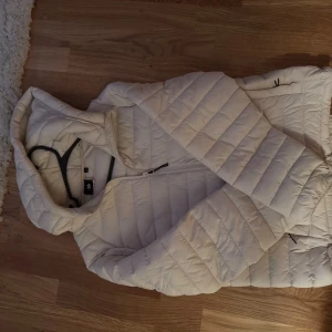 Beige quiltad pufferjacka med huva - Säljer en beige pufferjacka med huva och dragkedja framtill. Storlek M 