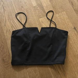 Svart croppad topp - Snygg svart topp med smala axelband och en cool V-ringad detalj framtill. Croppad passform som ger en stilren look. Perfekt att matcha med höga jeans eller kjol för en trendig vibe.