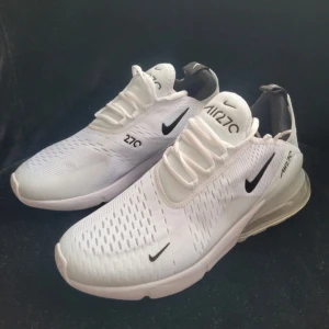 Nike Air Max 270 vita sneakers - Nike Air Max 270 sneakers i fräsch vit färg med svarta detaljer och synlig Air Max-bubbla i hälen. Ovandelen är tillverkad i ventilerande syntetmaterial med snörning och rund tå. Snygg och modern design som sticker ut med loggor på både sidor och plös.