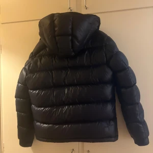Navy Moncler Maya - Svart pufferjacka från Moncler med stor huva, två sidofickor med dragkedja och Moncler-logga på ärmen. Jackan har en glansig finish och grova, quiltade sektioner. Dragkedjan framtill har Moncler-detaljer. Perfekt för kalla dagar. Pris kan diskuteras!! 