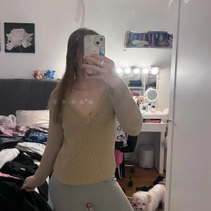 Beige stickad v-ringad tröja - Säljer en beige stickad tröja med v-ringning och långa ärmar. Tröjan har en klassisk, ribbad struktur och sitter normalt på kroppen. Perfekt för lager-på-lager under kyligare dagar.