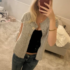 Grå stickad kofta med knappar - Mysig grå stickad kofta med korta ärmar och tre stora träknappar framtill. 