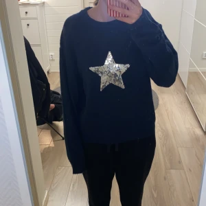 Mörkblå stickad tröja med paljettstjärna - Snygg mörkblå stickad tröja från Gina Tricot med en stor stjärna i glittriga paljetter på bröstet. Tröjan har rund hals och långa ärmar, perfekt för dig som gillar att sticka ut med coola detaljer.