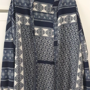 Klänning - Säljer en snygg blåvit klänning från Boohoo med unikt mönster i olika geometriska och blommiga former. Klänningen har långa ärmar och en lös passform, perfekt för dig som gillar bohemisk stil. Mjuk och skön mot huden. Lite nopprig