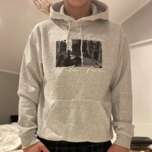 Montévas Vita Tua hoodie - Säljer en ljusgrå hoodie med svartvitt tryck på bröstet och texten 'Vita Tua'. Tröjan har huva med snörning och en stor magficka. Perfekt för dig som gillar streetstyle och vill ha en chill look.