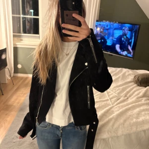 Svart skinnjacka med dragkedjor - Säljer en svart skinnjacka i mjukt tyg med silvriga dragkedjor och bälte i midjan. Jackan har dragkedja men är lika varm när den är nerdragen. Andvänt fårtal gånger men inget som syns, passar mig perfekt som brukar bära xs💕