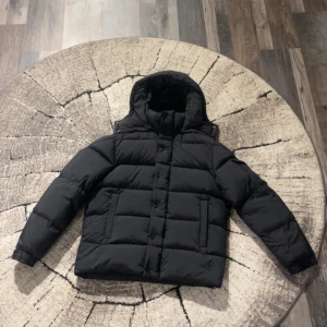 Svart Moncler Vezere - Svart pufferjacka från Moncler med ikonisk logga på ärmen, huva och grov dragkedja med Moncler-zip. Jackan har knappar framtill och quiltad design som ger en schysst volym. Insidan har en cool comic-strip etikett. Perfekt för kalla dagar. Varje knapp är detaljerad med monclers  egna loggotyp och huvan är avtagbar. Man får med moncler påse vid köp. Jackan är helt oanvänd och priset är flexibelt (diskuterbart)!  Storlek 3=M 