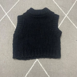 Svart stickad väst från NA-KD - Säljer en svart, chunky stickad väst från NA-KD i storlek XS. Västen har en hög krage och breda ribbade kanter vid ärmhål och nederkant. Perfekt att styla över en skjorta eller t-shirt för en trendig lager-på-lager-look.