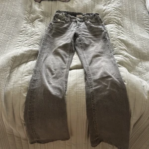 Grå jeansbyxor från Gina Tricot - Snygga grå bootcut jeansbyxor från Gina Tricot i storlek 158. Byxorna har utsvängda ben, coola detaljerade bakfickor med broderi och knapp med blomma. Klassisk femficksmodell och normal passform. Perfekta till en avslappnad stil.