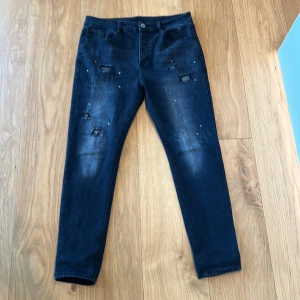 Svarata jeans med slitningar från KWD - Snygga svarta jeans från KWD med slitna detaljer och lite färgstänk framtill. Dom är använda 3 gånger så helt nya, Jeansen har klassisk femficksdesign, normal midja och smal passform. Perfekta för dig som gillar en streetig och trendig look. Jag är 190 och dom är bra i längden men sitter lite tajt på mig då ja har rätt breda lår, hör av dig vid intresse 