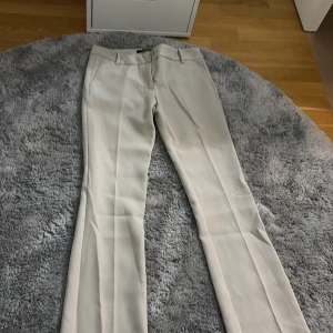 Beiga kostymbyxor från BikBok - Snygga beiga kostymbyxor från BikBok i klassisk rak modell. Byxorna har pressveck, hällor för bälte och sidfickor. Perfekta för en clean och stilren look. Materialet känns mjukt och har en lätt stretch för extra komfort.