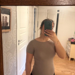 Beige topp med öppen rygg - Säljer en beige topp med korta ärmar och snyggt öppen rygg. Modellen är tight och har en enkel, stilren design utan mönster eller detaljer. Perfekt för dig som gillar minimalistisk stil och vill ha något som sticker ut med den öppna ryggen.