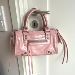 Rosa handväska med dragkedja - Snygg ljusrosa handväska i skinnimitation med silverfärgade nitar och detaljer. Perfekt storlek för det viktigaste och cool design som sticker ut. Endast använd fåtal gånger