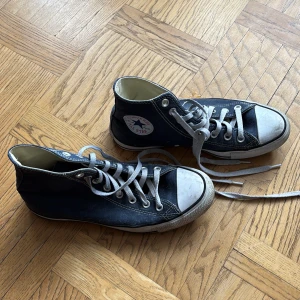 Converse All Star mörkblå high tops - Säljer ett par klassiska Converse All Star high tops i mörkblå canvas med vita gummidetaljer och rund tå. Skorna har snörning med gråa skosnören och den ikoniska loggan på sidan. Perfekt för dig som gillar retrostil och streetwear.