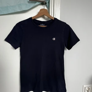 Mörkblå Champion t-shirt i bomull - Snygg mörkblå t-shirt från Champion med klassisk rund hals och korta ärmar. Diskret Champion-logga broderad på bröstet. Tillverkad i mjuk bomull som är skön mot huden och passar perfekt till jeans eller shorts.